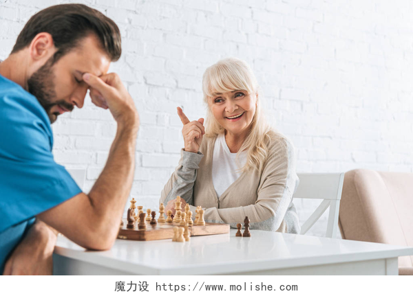 两个人下棋男的下输了微笑的资深妇女指向用手指和看不安的人在棋比赛以后